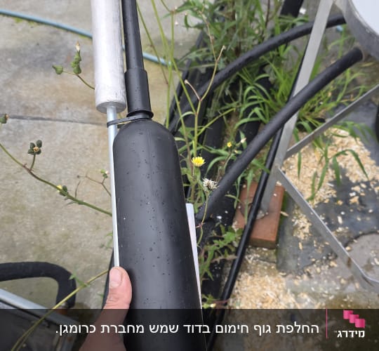 יד מחזיקה רכיב שחור של דוד שמש על רקע צמחייה